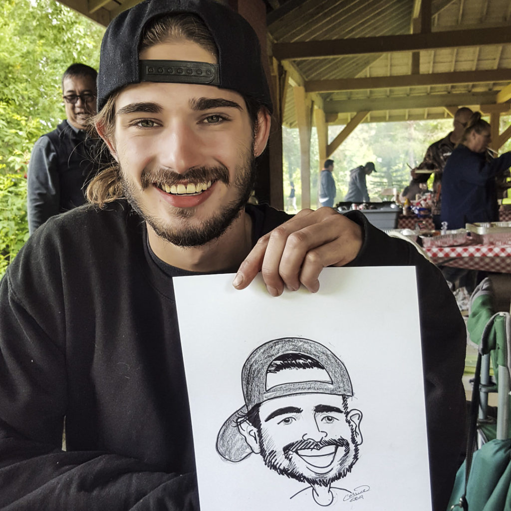 smiling man in a backwards ball cap holding a hand drawn caricature