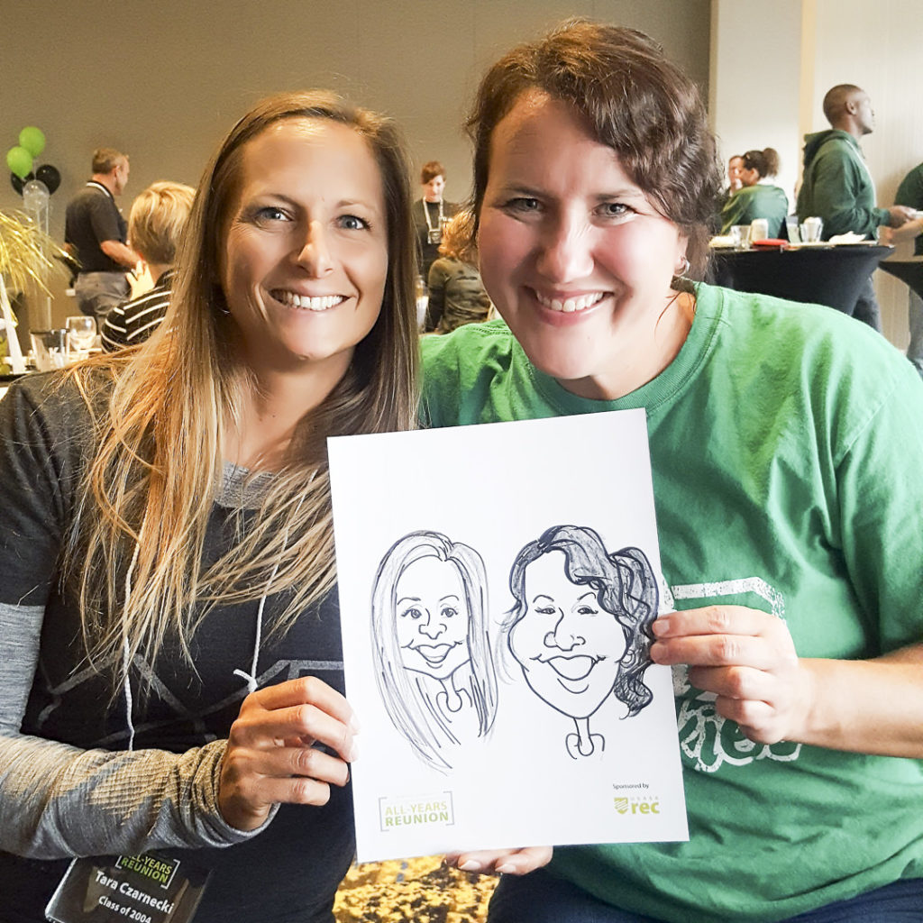 Two friends at U of S Reunion in Saskatoon, Saskatchewan hold up caricature art