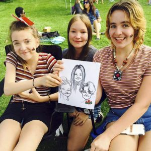 Three girls with drawing of themselves at an outdoor event in Saskatoon